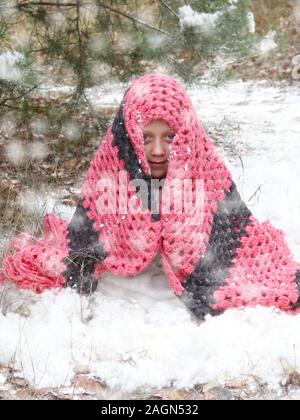 Petite fille congelé dans la forêt d'hiver. jeune fille dans la forêt d'hiver, assis, enveloppé dans une écharpe, essayant de garder au chaud Banque D'Images