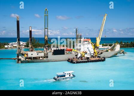 Le bateau en bois en passant par le navire avec des grues industrielles qui travaillent dans le port de Nassau, près de Paradise Island (Bahamas). Banque D'Images