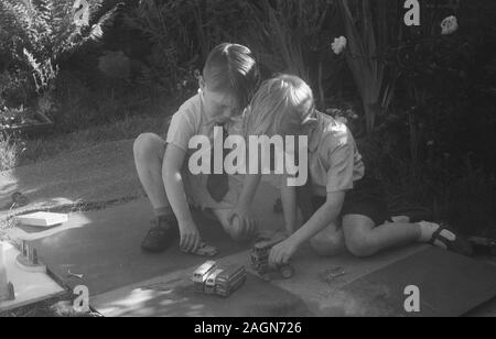 Années 1950, historiques, deux petits garçons jouent ensemble avec metal toy bus, à l'extérieur sur un patio, England, UK. Banque D'Images