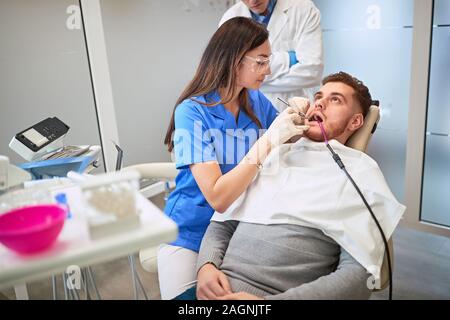 Jeune homme dans le fauteuil dentaire au dentiste femelle Banque D'Images