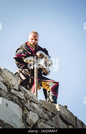 Un homme dans un costume d'un chevalier médiéval avec une hache sur le mur d'une forteresse. Banque D'Images