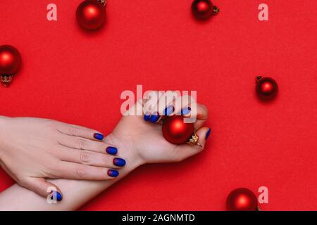 Femme parfaite avec les mains manucure tendance holding Christmas jouet sur fond rouge. Banque D'Images