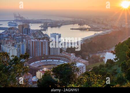 Soleil profond à l'horizon sur Malaga. La ville sur la Costa del sol espagnole au coucher du soleil avec vue panoramique sur le port, maisons, arbres, arènes Banque D'Images