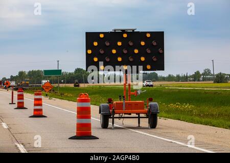 Un gros plan d'une matrice mobile LED garder la gauche signe, avec des feux clignotants orange les automobilistes d'avertissement avec des flèches et des cônes routiers au cours de fermeture de voie Banque D'Images