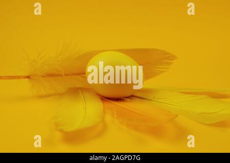 Oeufs de Pâques une couleur et plume sur fond jaune. Joyeuses Pâques carte de vœux. Un minimum d'easter concept. Banque D'Images