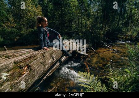 Belle jeune fille s'assied sur se connecter, et après un voyage. Woman traveler en été passe sur pont en bois en arrière-plan de forêt. Comblé se trouve sur la rivière. Banque D'Images