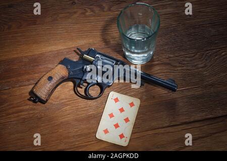 Roulette russe - huit de carreau carte plaing, verre de vodka et revolver avec une cartouche de tambour sur fond de table en bois Banque D'Images