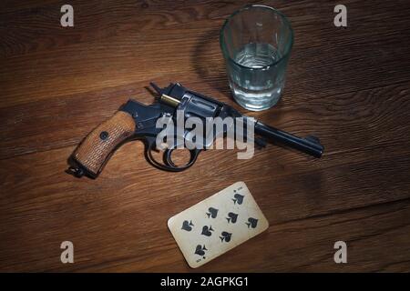 Roulette russe - huit de pique carte plaing, verre de vodka et revolver avec une cartouche de tambour sur fond de table en bois Banque D'Images