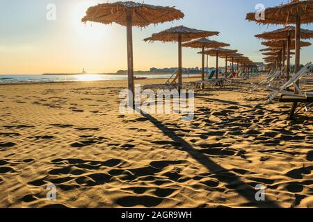 Coucher de soleil sur la plage avec parasols et chaises longues: Convento ou San Lorenzo plage est situé à proximité de Vieste dans les Pouilles, en Italie. Banque D'Images