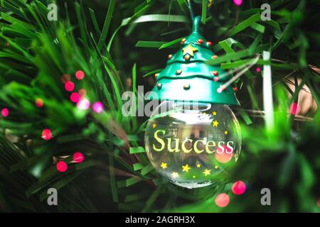Close-up globe de verre avec le mot succès accroché dans l'arbre de Noël. Banque D'Images