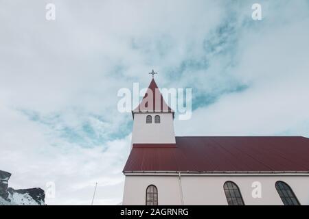 Photo sous angle d'un bâtiment religieux au toit rouge avec un croix sur le dessus sous un ciel bleu nuageux Banque D'Images