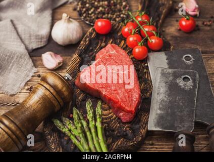 Tranche de boeuf cru sirlion steak sur planche en bois avec des tomates, l'ail et les asperges et la viande hache sur la table de cuisine et arrière-plan. Banque D'Images