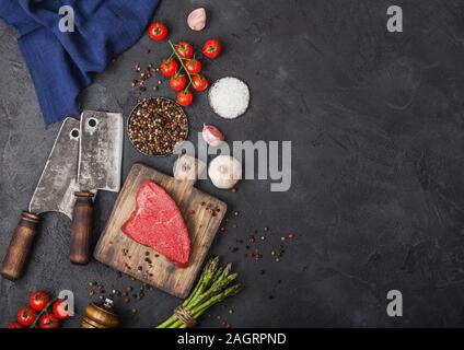 Tranche de boeuf cru sirlion steak sur planche en bois avec des tomates, l'ail et les asperges et la viande hache sombre sur fond de table de cuisine. Banque D'Images