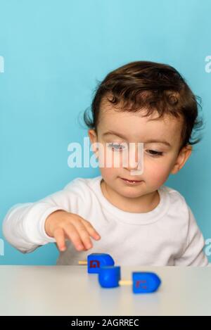 Cheveux bouclés juif gentil petit garçon jouant avec la couleur bleue classique au dreidel maison. Banque D'Images