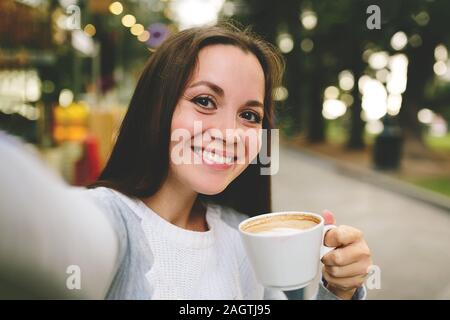 Belle jeune fille avec une prise de café et fait en selfies street cafe. Banque D'Images