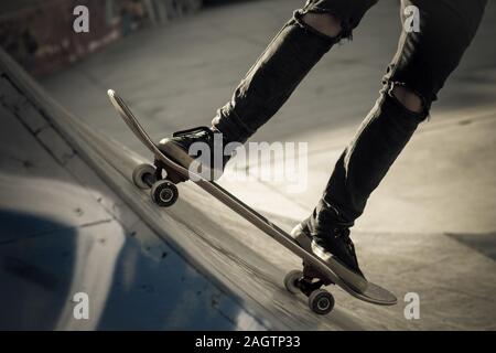 Vue rapprochée de tennager's pieds équitation un skateboard faisant des tours sur demi-lune. Quartier branché de jeunes patineurs bénéficiant d'extérieur au skatepark avec patinage boa Banque D'Images