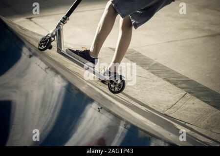 Vue rapprochée de tennager's pieds de la trottinette fait des tours sur un half pipe. Quartier branché de jeunes patineurs bénéficiant d'extérieur au skatepark avec scooter de coup Banque D'Images