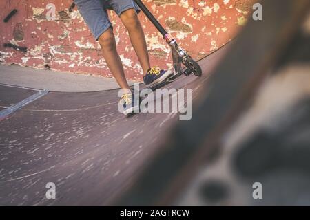 Vue rapprochée de tennager's pieds de la trottinette fait des tours sur un half pipe. Quartier branché de jeunes patineurs bénéficiant d'extérieur au skatepark avec scooter de coup Banque D'Images