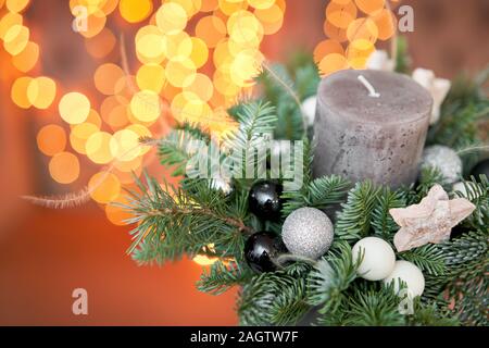 Petit arrangement de l'épinette fraîches avec une bougie dans un pot en céramique. Ambiance de Noël. Des phares sur Garland flou d'arrière-plan. Banque D'Images