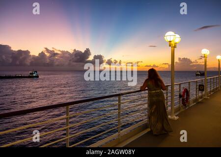 Regarder une femme, à partir d'un grand bateau de croisière luxueux amarré dans un port au cours d'un ciel nuageux et soleil colorés. Prises à Bridgetown, à la Barbade. Banque D'Images