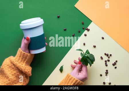 Café concept zéro déchet. Eco friendly tasses à café réutilisables dans les mains. Télévision géométrique jeter sur split two tone de papier. Arrière-plan créatif en vert, orang Banque D'Images