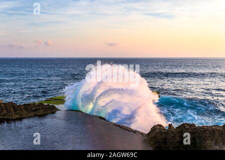 Vague d'arc-boutement se briser contre falaise à la déchirure du diable, sur la côte de Nusa Lembongan, à Bali, Indonésie. Piscine de l'eau sur le haut de falaise en premier plan. Banque D'Images