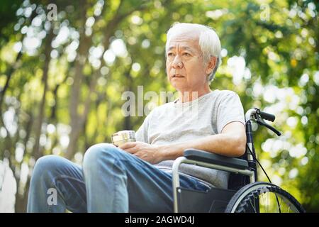 Triste homme asiatique assis en fauteuil roulant à l'extérieur Banque D'Images