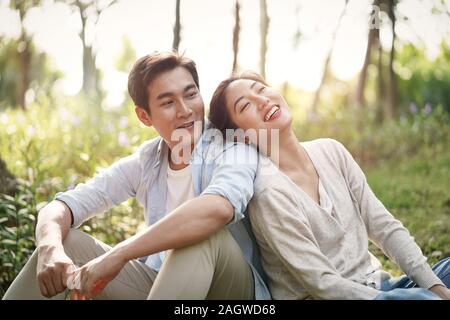 Beautiful happy young asian woman sitting on grass talking chatting relaxing in park Banque D'Images