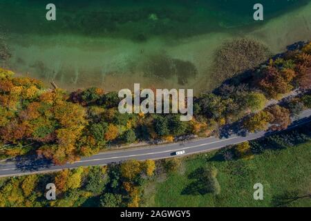 Vue aérienne de route avec une voiture à l'automne forêt à côté d'un touquise lac de couleur. Banque D'Images