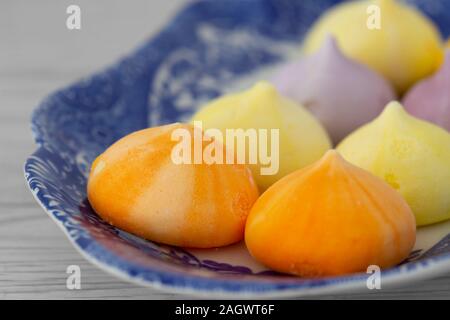 Meringues, différentes couleurs, sur une assiette blanche et bleu à motifs. Fond en bois gris Banque D'Images