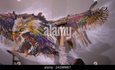Concepteur de l'artiste dessine un aigle sur le mur. Décorateur artisan photo peintures à l'acrylique couleur d'huile. Peintre peintre vêtu de couche de peinture. À l'intérieur. Banque D'Images