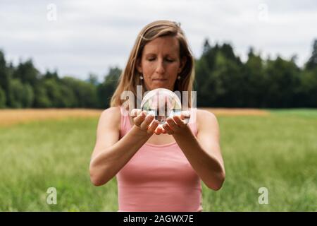 Jeune femme tenant dans ses mains une boule de cristal se trouvait à l'extérieur dans une nature magnifique. Banque D'Images