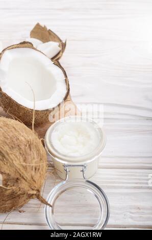 L'huile de noix de coco dans un bocal en verre hermétique et les plaques sur la table en bois blanc libre Banque D'Images