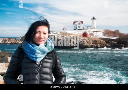 Une femme chinoise voyageant en Amérique latine avec le Cape Neddick lighthouse nubble à l'arrière du terrain dans Cape Neddick Maine le ciel bleu ensoleillé une journée d'hiver. Banque D'Images