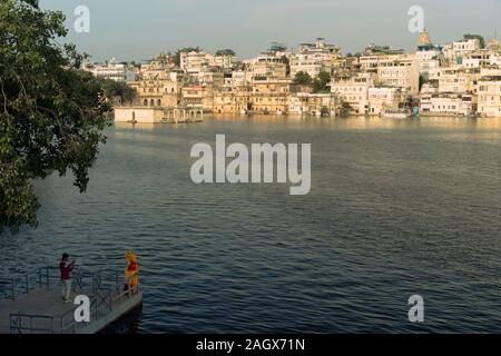Le lac Pichola avec couple photographier et de bâtiments anciens dans la distance un soir d'été à Udaipur, Rajasthan, Inde. Banque D'Images