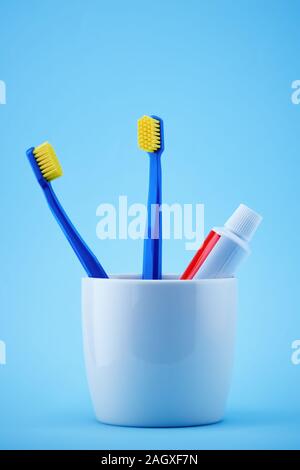 Des brosses à dents et un tube de dentifrice dans un porte-tasse contre fond bleu. Soins dentaires Banque D'Images