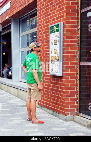 Montréal, Canada - Juin 2018 : Young man looking at les éléments de menu d'un restaurant sur la rue à Montréal, Québec, Canada Banque D'Images