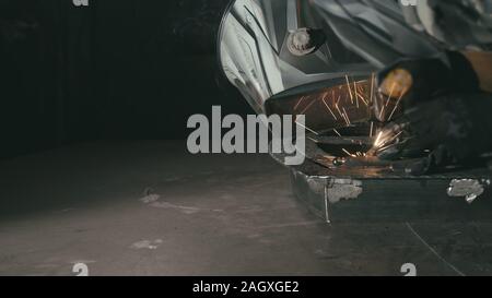 Atelier de forge. Smithy. Travailleur dans une hotte de soudure soudure casque une partie par soudure électrique. Des étincelles se reflètent dans l'écran de protection. Banque D'Images