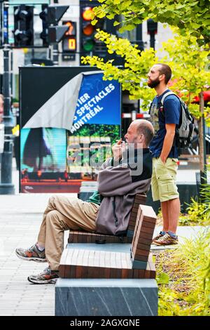 Montréal, Canada - Juin 2018 : l'homme sans-abri assis sur le banc et de cigarette avec une jeune Canadienne hipster se tenant derrière lui. Banque D'Images