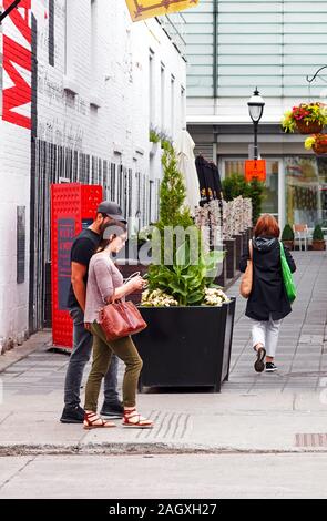 Montréal, Canada - Juin 2018 : Jeune couple canadien marche sur la rue et à la recherche à leur smartphone à Montréal, Canada. Banque D'Images