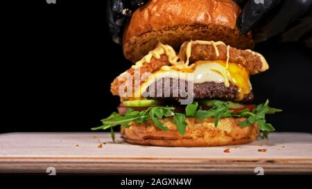 Burger d'artisanat est cuisson sur fond noir. Composé : sauce, roquette, tomate, oignon rouge, de concombre, de frites, de fromage et de pain de viande en l'air de boeuf. Banque D'Images