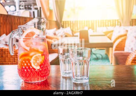 Pichet avec du jus d'orange et deux verres vides sont debout sur une table dans un café sur une chaude journée ensoleillée. L'espace de copie pour le texte. Banque D'Images