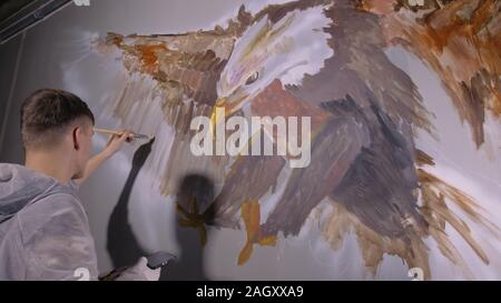 Concepteur de l'artiste dessine un aigle sur le mur. Décorateur artisan photo peintures à l'acrylique couleur d'huile. Peintre peintre vêtu de couche de peinture. À l'intérieur. Banque D'Images