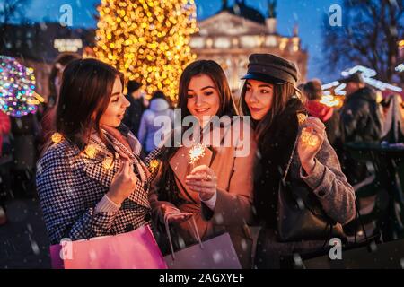 Nouveau concept de l'année. Les femmes amis brûler des cierges merveilleux à Lviv par arbre de Noël sur foire de rue. Girls holding shopping bags Banque D'Images