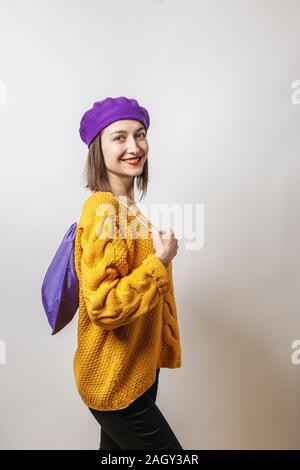 Portrait of young smiling woman wearing sweater jaune et violet, béret violet sac textile holding Banque D'Images
