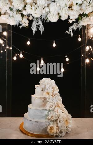 Gâteau de mariage blanc avec des pivoines et roses fleurs sur la cérémonie de nuit à l'extérieur. Très grand gâteau de mariage à trois niveaux avec crème au beurre blanc Banque D'Images