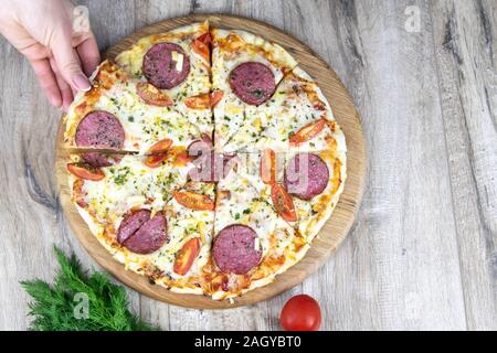 La main de la femme prend un morceau de pizza à partir de la ronde en bois stand Banque D'Images