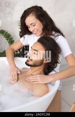 Young smiling woman making massage de la poitrine de son mari dans la baignoire relaxante Banque D'Images