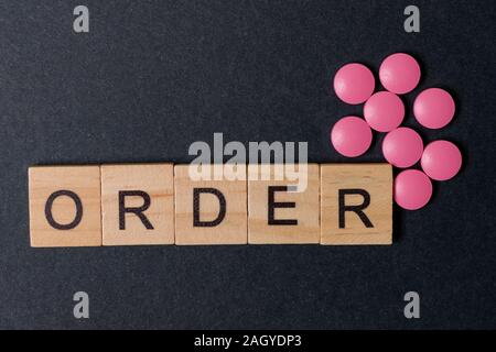 Pilules roses et de places à l'ordre des mots sur fond de papier noir. Concept de l'achat de médicaments. Banque D'Images