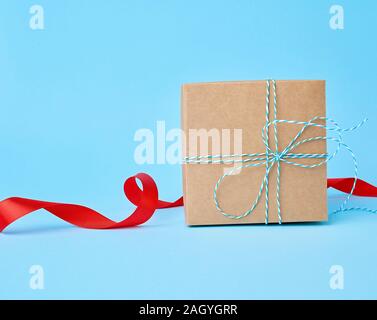 Boîte en carton brun carré pour un cadeau et torsadées ruban rouge en soie sur un fond bleu. Fort beau cadeau, grand design pour tout usage. Banque D'Images